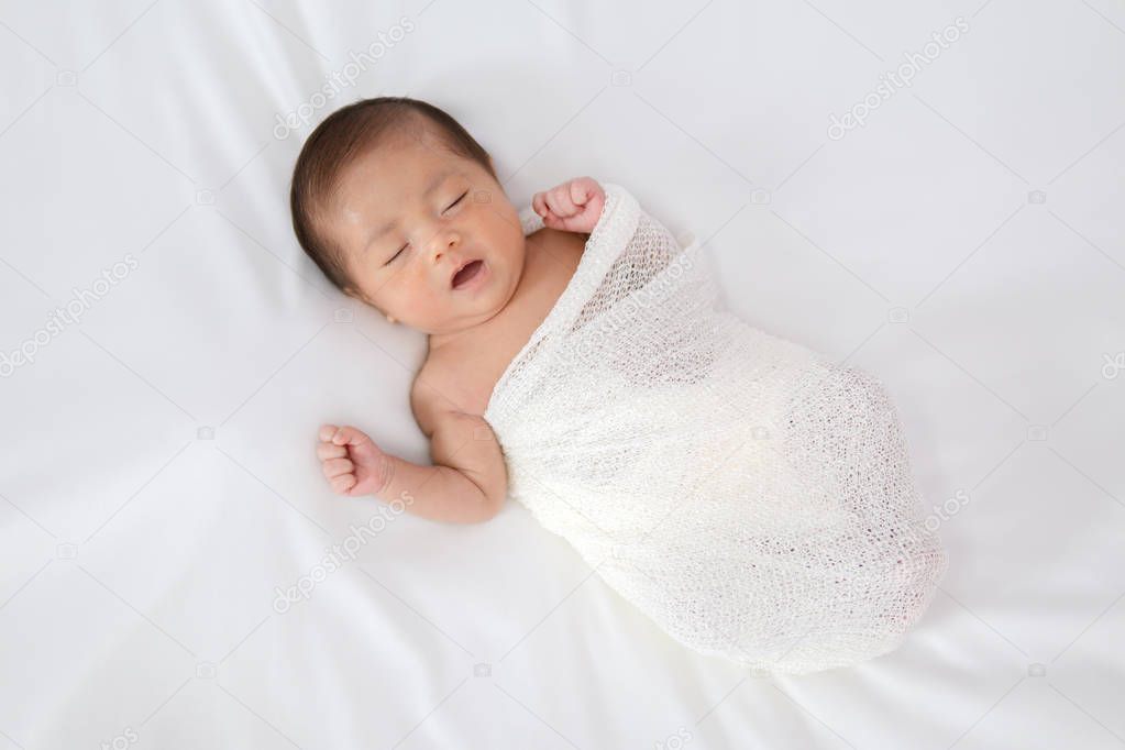 Sleeping newborn baby in white wrap while on white blanket backg