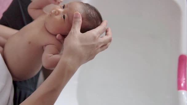 幸せと笑顔のアジアの新生児は白いプラスチック製の浴槽でお風呂に入っています お父さんは 彼女の顔を洗い バスルームで入浴小さな赤ちゃんを保持しています 乳幼児の洗濯 衛生と赤ちゃんの世話 — ストック動画