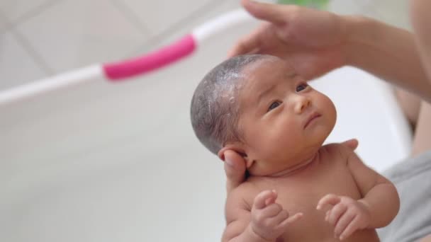 愛らしいアジアの新生児の女の子は オーガニックシャンプーで髪を洗い 自宅のバスルームで白いプラスチック製の浴槽で彼女の父親によってお風呂を取っています ベビー用品 新生児の衛生と健康管理 — ストック動画