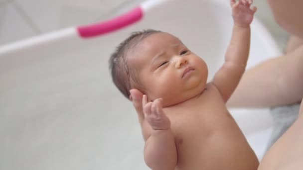 愛らしいアジアの新生児の女の子は 自宅のバスルームで白いプラスチック製の浴槽で髪を洗い 彼女の父親によってお風呂に入っています 新生児の洗濯と入浴 衛生と健康管理 — ストック動画