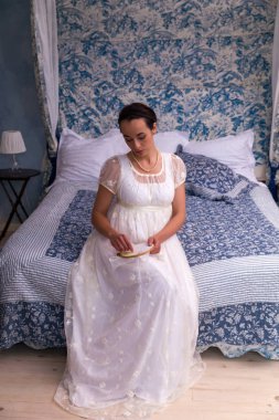 Antika bir yatağa oturmuş otantik regency elbiseli çekici genç kadın