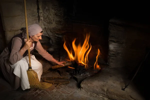 Средневековая горничная добавляет дров в огонь — стоковое фото