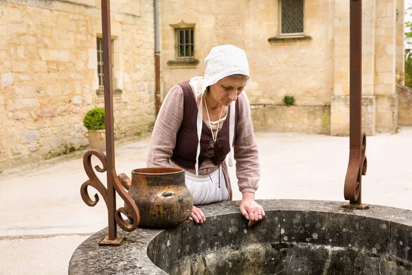 在法国中世纪城堡的一口老井工作的身着历史性服装的妇女 — 图库照片