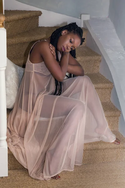 Pretty young woman in sheer nightgown sitting on stairs