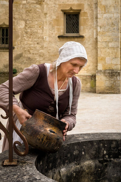 Woman in historic outfit working at an old water well of a French medieval castle