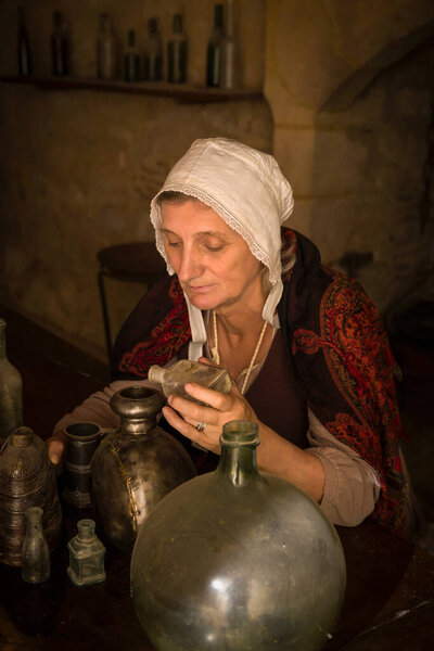 Woman in medieval outfit working as an alchemist or witch in the kitchen of a French medieval castle