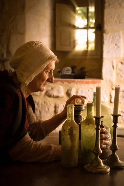 Woman in medieval outfit working as an alchemist or witch in the kitchen of a French medieval castle