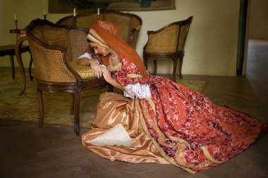 Young woman in medieval renaissance costume and French hood sitting on the floor holding a letter