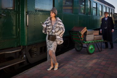 1927 model birinci sınıf bir tren vagonunun yanındaki platformda canlandırma sahnesinde 1920 'lerden kalma lüks bir bayan valizini bekliyor.