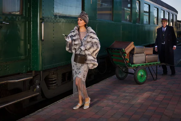 1927 model birinci sınıf bir tren vagonunun yanındaki platformda canlandırma sahnesinde 1920 'lerden kalma lüks bir bayan valizini bekliyor.