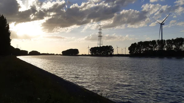 Sonnenuntergangssilhouette Ufer Eines Kanals Industriegebiet Windkraftanlage Und Strommast Der Ferne — Stockfoto