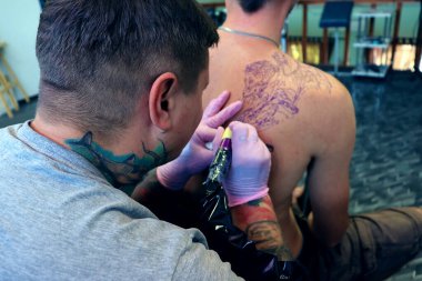 Güzel bir dövme salonu geçmişi var. Dövme sanatçısı erkek derisine çizim yapıyor