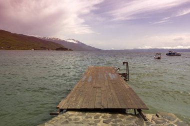 Teknelerle Ohri Gölü'ne ahşap bir köprüden manzara. Hafif bulutlu bir gökyüzünün arka planına karşı gün batımında. Makedonya.