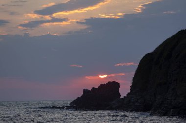 Yükseldikten sonra, güneş kayanın üzerindeki bulutlara doldu. Sinemorets tatil beldesinden görünüm, Güney Karadeniz Kıyısı, Bulgaristan.