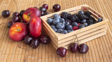 Doğanın armağanları. Ahududu, kiraz, yaban mersini, böğürtlen ve düz nektarin. Bir paspas üzerinde küçük bir sandık içinde.