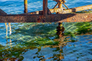 Denizin berrak sularına pas ile kaplı metal yapının bileşimi yansıyor..