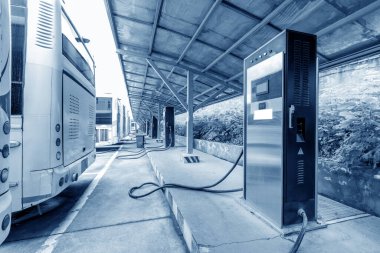 Bir otobüsün arka planında elektrikli bir arabanın şarj istasyonu.