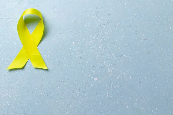 Yellow ribbon on a blue cement  background.World suicide prevention day.