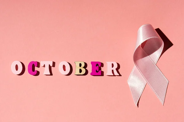 OCTOBER word and pink ribbon on pink background.Breast cancer. — Stock Photo, Image