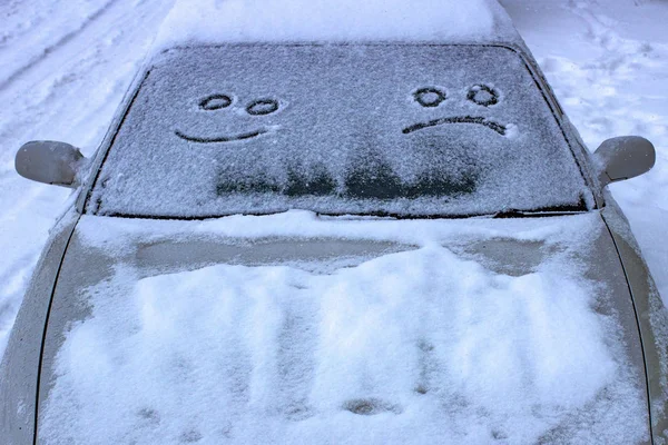 the sad and the happy smile on the snowy windshield of a car