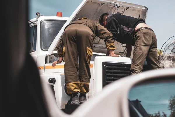 men repairing a truck with manual labor under the open hood with a hand tool, engine accident on a long journey