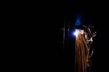 Kaynak işi yapan bir adam, bir ark manuel aparatıyla karanlıkta.