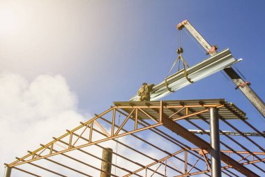 Mobil vinç, damak damağındaki metal çatı örtüsünü kaldırıyor. İnşaat alanında çelik yapı çatı kirişine bağlanıyor.