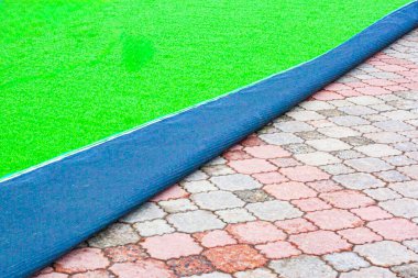 Şiddetli rüzgar ve acil durumlarda yırtılmayı önlemek için çekiç matkabıyla kaldırım levhalarının üzerine yeşil yapay çim kurulması