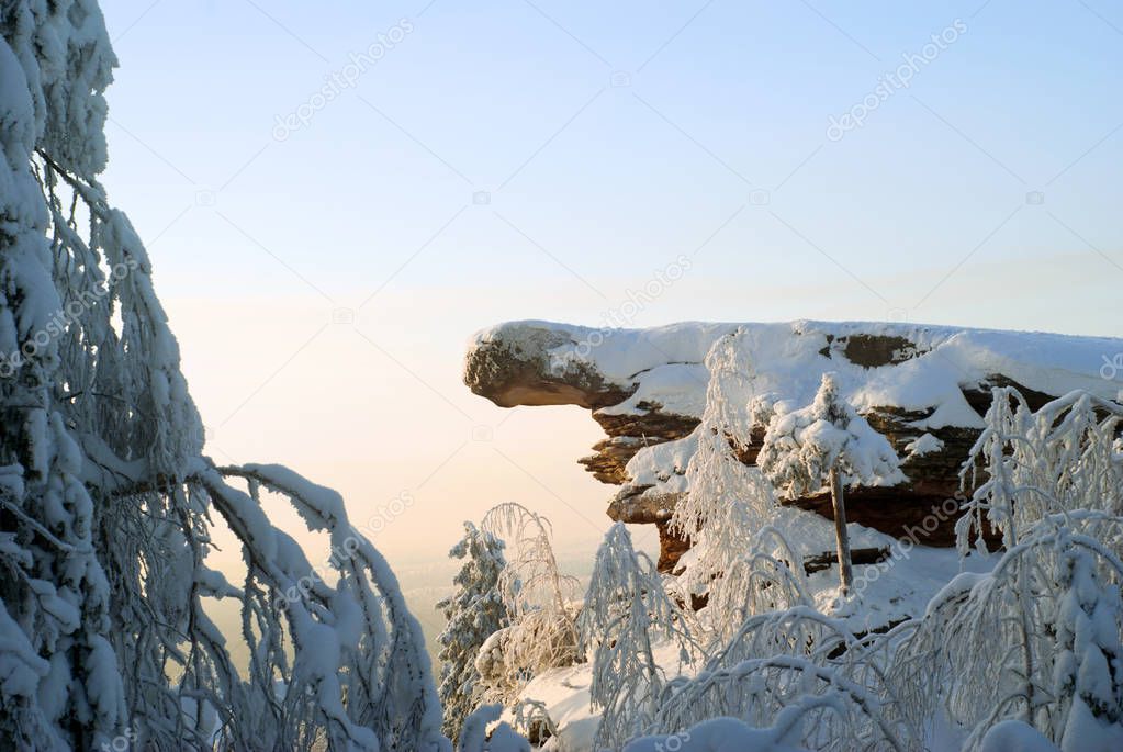 a sandstone rock surrounded by snow-covered trees on top of a mountain in a frosty winter sunny day