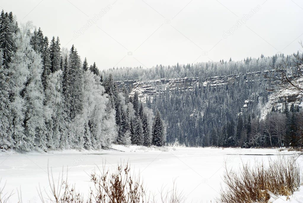 winter landscape with a frozen mountain river between high cliffs, covered with coniferous forest