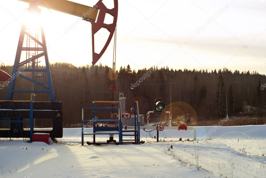 a bright pumpjack over an oil well in a winter snowy forest landscape