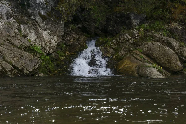 The spring follows a waterfall from the rock and flows into the river on a precipitous river ban