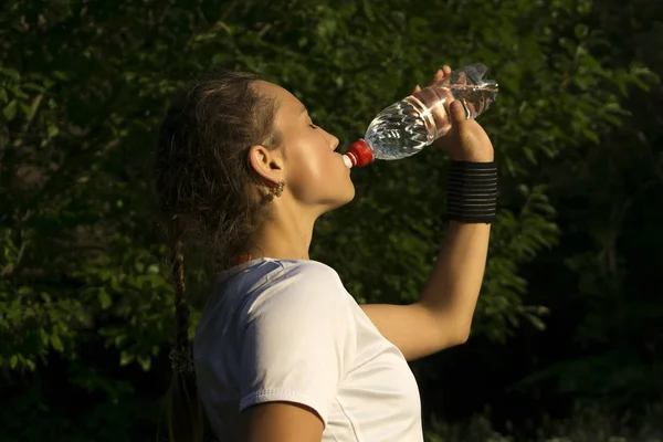 girl after playing sports in the park quenching thirst drinks water from the bottle