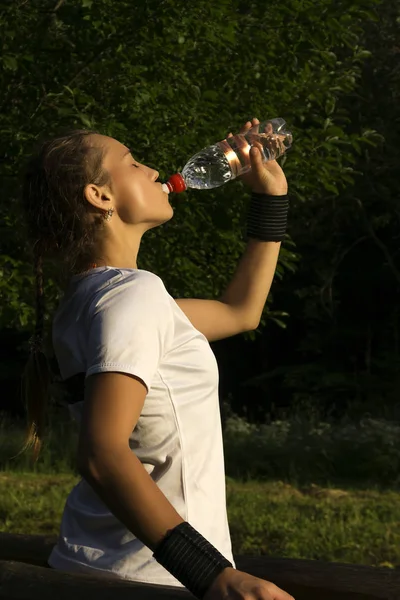 girl after playing sports in the park quenching thirst drinks water from the bottle