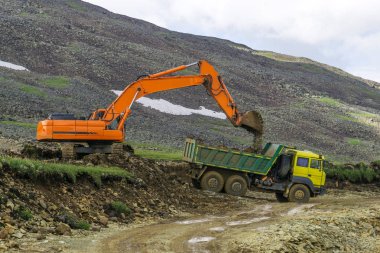 Dağlık bir alanda, bir ekskavatör ve bir damper bir yol inşaat çalışmaları sırasında döşeme