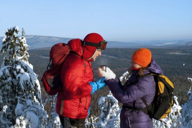 İki yürüyüşçü orman manzara Vadisi zemin karşı açık soğuk bir gününde dağın zirvesinde; bir kadın bir adam bir fincan (şapkalı bir termos sıcak bir çay sunar.).
