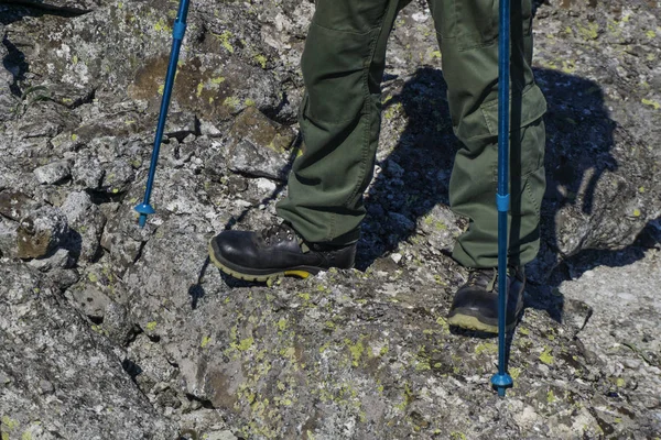 feet of a man in hiking boots with trekking poles walking in a rocky landscap