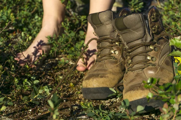 pair of taken off trekking boots in the foreground and bare feet of a resting woman on the grass in the background