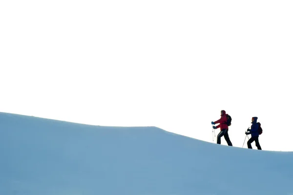 バックパックや北部散歩に棒で二人は 空が白い雪に覆われた斜面の尾根に沿って歩いています — ストック写真