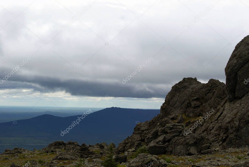 mountain landscape of the North Urals in summer in cloudy weather with a wrinkled, bumpy rock in the corner in the foregroun