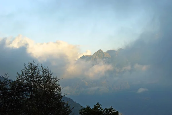 雲の間太陽に照らされた山の頂上に 日陰では谷の反対側にある山の斜面からの夕景 — ストック写真