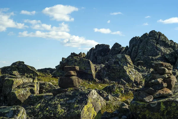 stone pyramid - a road sign for the designation of a trail in the fog - in a beautiful mountainous wild terrain with picturesque rocks under a blue sky