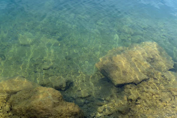 きれいな山の湖の海岸の反射と透明な緑がかった水の背景 ストック写真