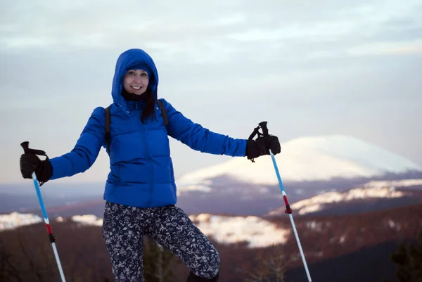 traveler girl in warm clothes with poles for a nordic walking in hands against a background of a dawn winter blurry mountain landscape