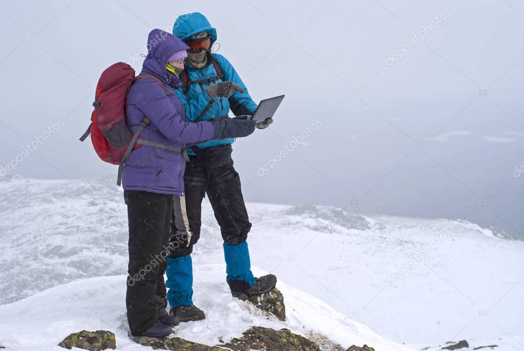 two hikers on a winter mountain peak with a laptop