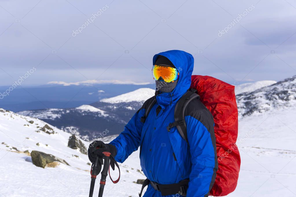 mountaineer in mirror wind-proof glasses and a windproof mask with a backpack on a background of a winter mountain landscape