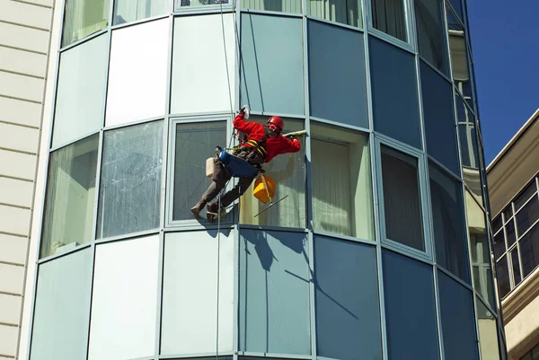 worker in a helmet washes the window of a high-rise building from the outside, hanging on a rope