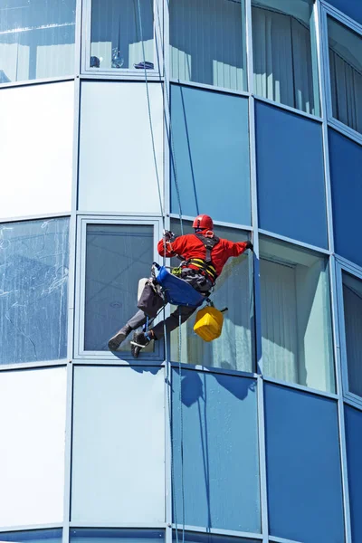 rope access technician in a helmet washes the window of a high-rise building from the outside, hanging on a rope