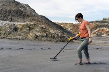 kadın çamur ıssız bir vadide ayak bileği-derin bir metal dedektörü ile arama yapar.