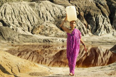 kız bir sari oryantal görünüm başına su ile büyük bir plastik tüp çöl bir alana taşır